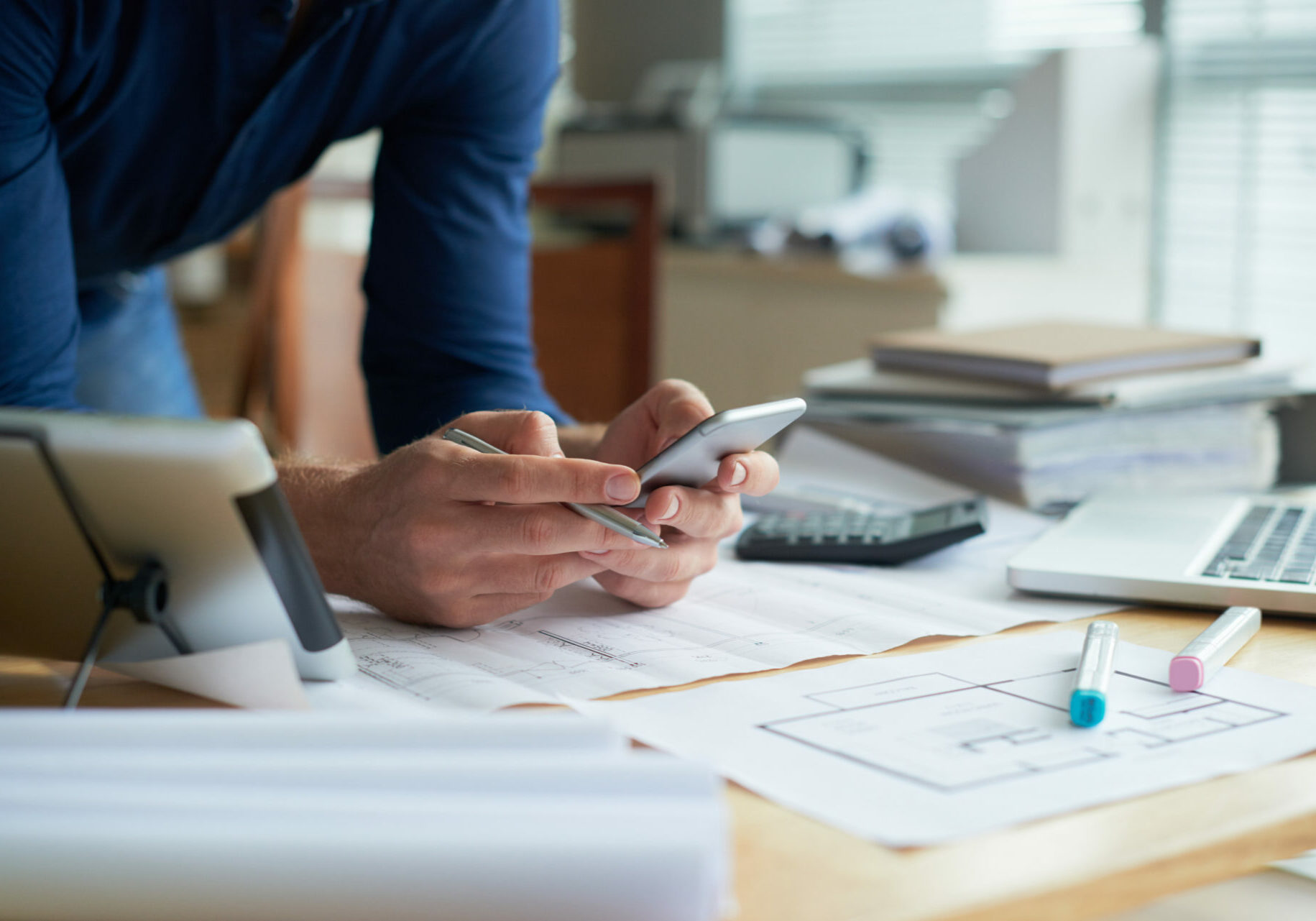 Architect leaning on table with blueprints and reading text messages